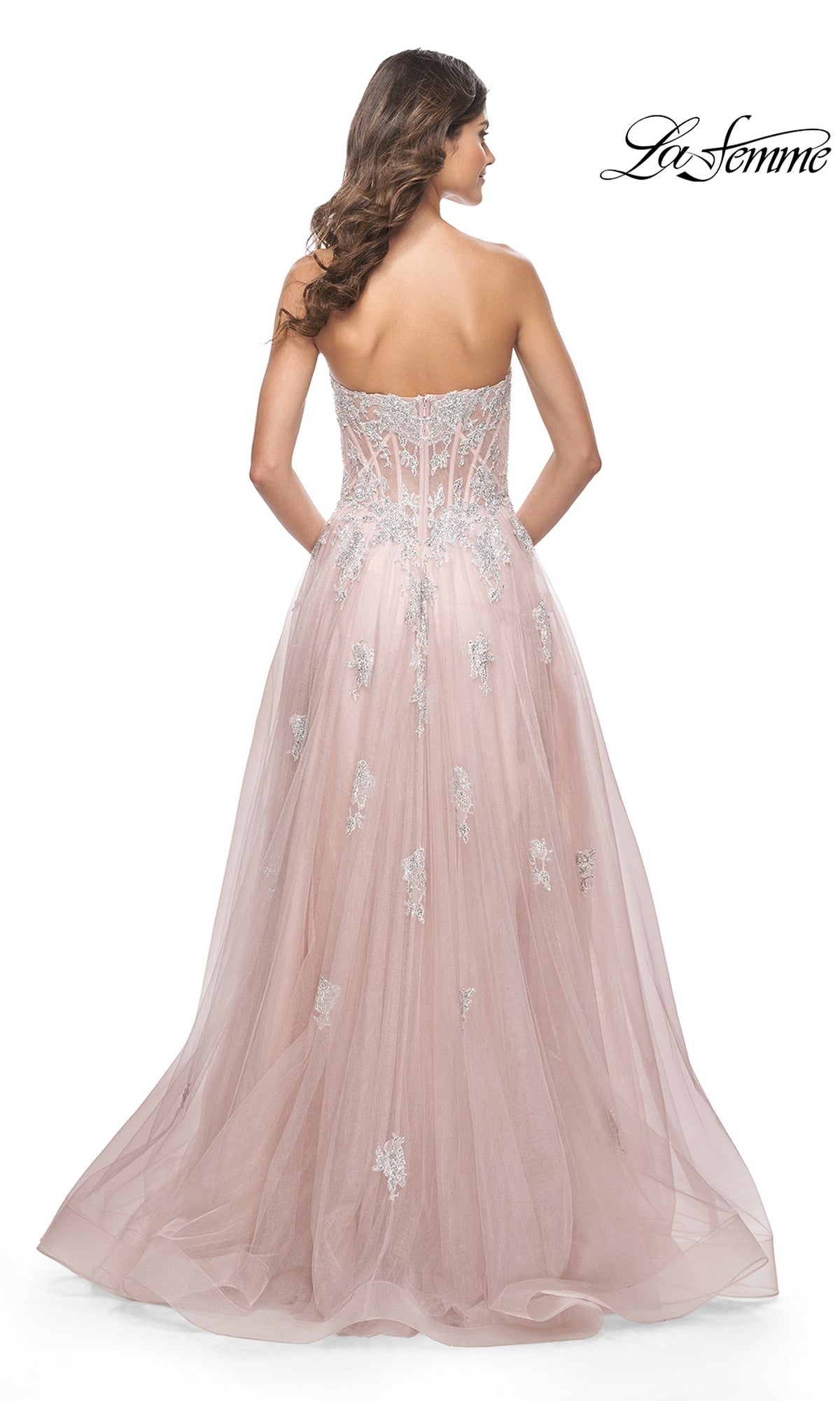 A woman in the La Femme Strapless Long A-Line Prom Dress 32111, with blush pink fabric and silver lace appliques, is seen from the back against a white background.
